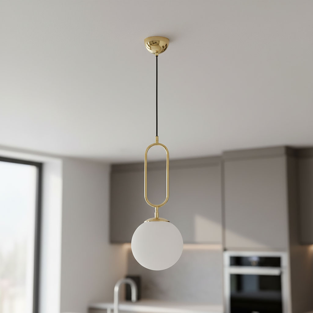 Lampa wisząca Vavil D200 w złotym kolorze z białym kloszem w kształcie kuli, zawieszona na czarnym przewodzie. Widok z góry, w nowoczesnej kuchni z szarym tłem i blatem.