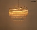 Lampa wisząca Luma 60 w kolorze złotym, o konstrukcji z przezroczystych elementów. Posiada dziewięć miejsc na żarówki E14, zawieszona na łańcuchu, w górnej części o zaokrąglonym kształcie, emitująca ciepłe światło. Tło proste.