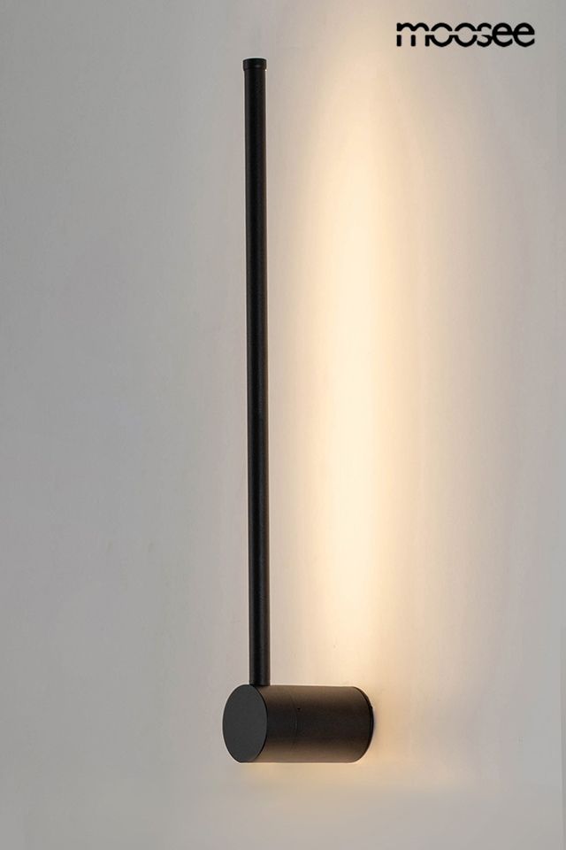 Kinkiet Ombre 60 LED w kolorze czarnym, z prostą, cylindryczną podstawą i długim, wąskim ramieniem, emitującym ciepłe światło. Zawieszony na ścianie, tworzy minimalistyczny efekt oświetleniowy. Tło jasne, podkreślające formę lampy.