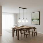 Lampa wisząca Sitro w kolorze czarnym i białym, z trzema okrągłymi kloszami, zawieszona na prostokątnej listwie. Ujęcie z boku, w aranżacji jadalni z drewnianym stołem i krzesłami. Tło jasne, z widoczną sztuką na ścianie.