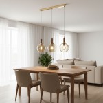 Lampa wisząca Hetty z trzema szklanymi kloszami w kolorze złotym i drewnianymi elementami, zawieszona na prostokątnej podstawie. Widoczna w aranżacji jadalni nad drewnianym stołem, z czterema krzesłami i rośliną w tle.
