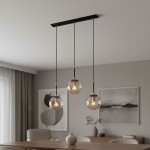 Lampa wisząca Sebia 3-punktowa z trzema szklanymi kloszami w kształcie kul, zawieszona na czarnych linkach. Elementy metalowe w kolorze złotym. Lampa umieszczona nad drewnianym stołem w nowoczesnym wnętrzu.