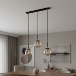 Lampa wisząca Sebia 3-punktowa z trzema szklanymi kulami w kolorze przezroczystym, zawieszona na czarnych linkach. Metalowa podsufitka w kolorze czarnym. Produkt umieszczony w nowoczesnym wnętrzu z drewnianym stołem i dekoracjami.