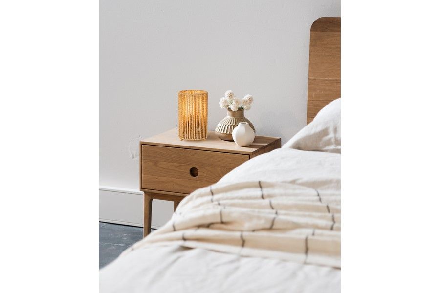 Lampa stołowa Tensa 1xE27 w kolorze czarnym i brązowym, z cylindrycznym kloszem w odcieniach brązowych, umieszczona na drewnianej szafce nocnej obok dekoracyjnych wazonów i kwiatów, w aranżacji sypialni.