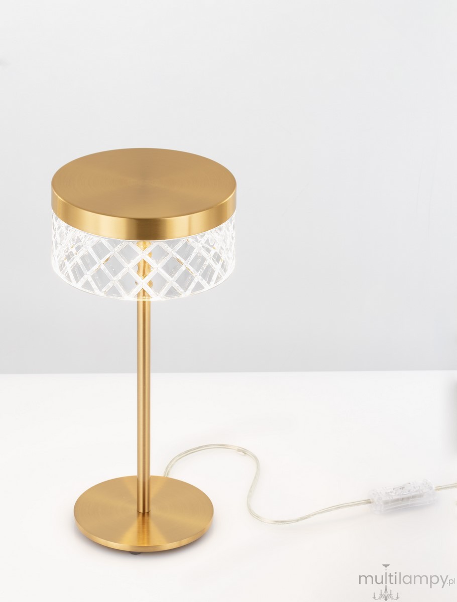 Lampa stołowa Mineros z jednym źródłem LED 6W, złota, z okrągłym, matowym kloszem i dekoracyjnym, przezroczystym abażurem o diamentowym wzorze. Ustawiona na płaskiej podstawie, z widocznym kablem zasilającym.