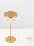 Lampa stołowa Mineros z jednym źródłem LED 6W, złota, z okrągłym, matowym kloszem i dekoracyjnym, przezroczystym abażurem o diamentowym wzorze. Ustawiona na płaskiej podstawie, z widocznym kablem zasilającym.