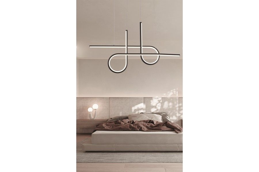 Lampa wisząca LED Barrel 32W CCT w kolorze czarnym, o nowoczesnym kształcie z płaskimi, zakrzywionymi elementami. Zawieszona nad łóżkiem w jasnym wnętrzu, na tle szarej ściany i beżowego łóżka z pościelą.
