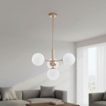 Lampa wisząca Volda Picolo 4-punktowa w kolorze złotym z czterema okrągłymi, matowymi kloszami. Produkt zawieszony na cienkim drucie, umieszczony w jasnym wnętrzu z szarym sofą i stołem.