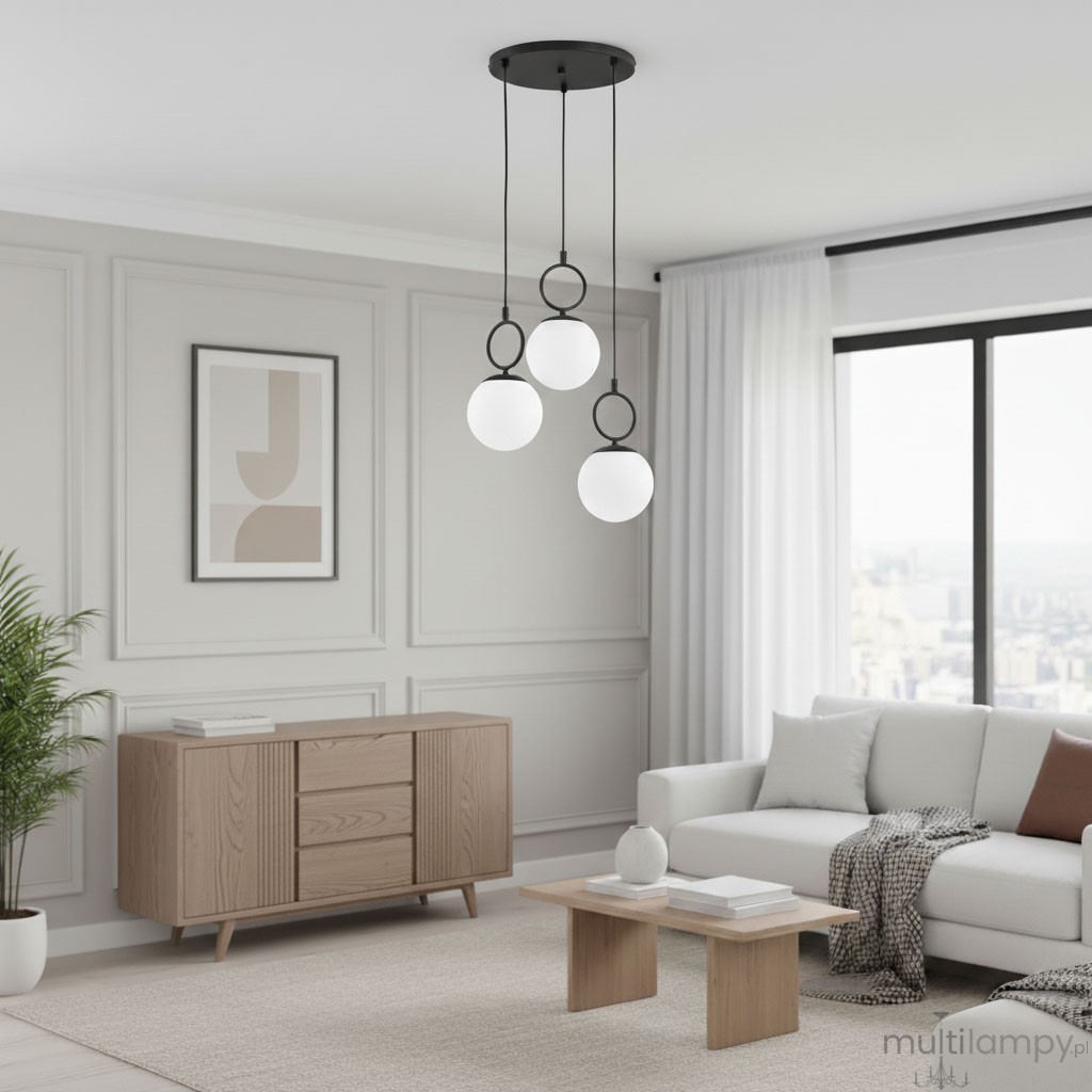 Lampa wisząca Sitro 3xE14 w kolorze czarnym i białym z trzema okrągłymi kloszami zawieszonymi na cienkich linkach. Umieszczona na prostokątnej podstawie sufitowej, w nowoczesnym wnętrzu z jasnymi ścianami i drewnianymi meblami.