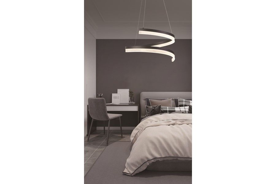 Lampa wisząca LED Manacor 28W CCT w kolorze czarnym, z unikalnym, falistym kształtem. Powieszona nad łóżkiem w sypialni, z jasnym światłem. W tle widoczna szara tapicerka oraz biurko z rośliną doniczkową.
