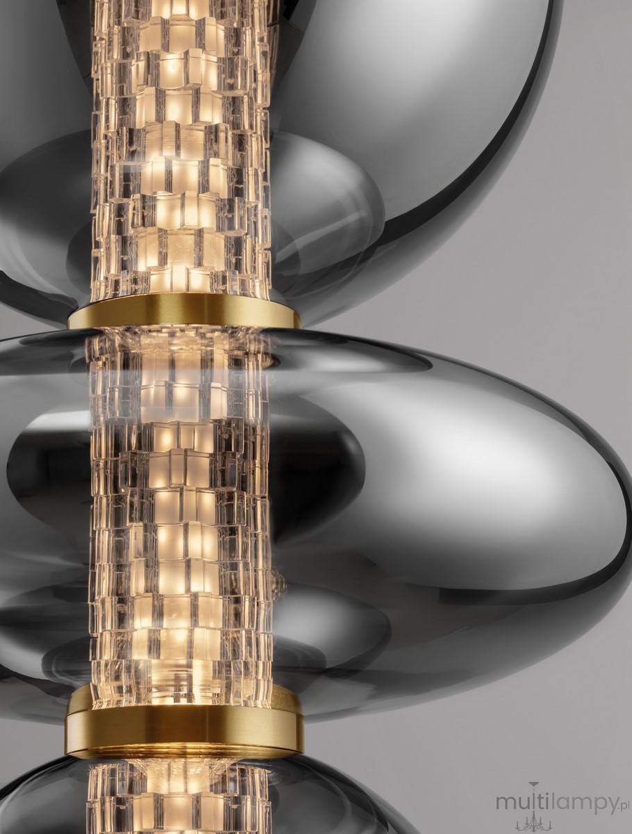 Lampa wisząca Morros z jednym źródłem LED 20W. Elementy w kolorze złotym, przezroczyste klosze o zaokrąglonym kształcie z teksturowanym wnętrzem. Widoczny centralny element świetlny, zawieszony na tle szarym.