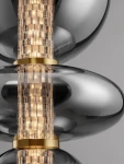Lampa wisząca Morros z jednym źródłem LED 20W. Elementy w kolorze złotym, przezroczyste klosze o zaokrąglonym kształcie z teksturowanym wnętrzem. Widoczny centralny element świetlny, zawieszony na tle szarym.