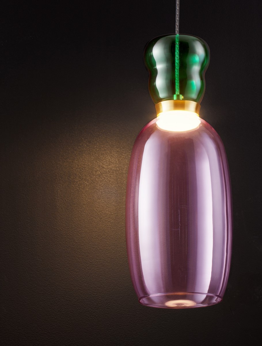 Lampa wisząca Perene z jedną żarówką LED 9W, o kształcie butelki z fioletowego szkła, z zielonym akcentem na górze i złotym detalem u podstawy. Zawieszona na cienkim przewodzie, na ciemnym tle.