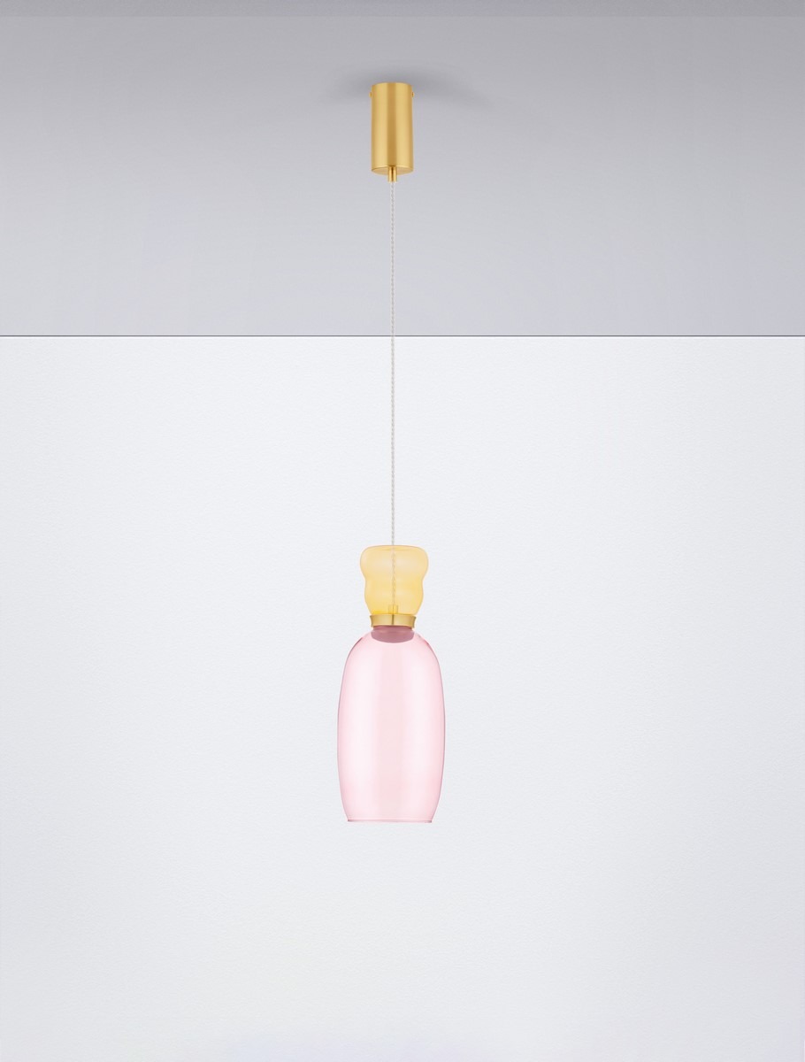 Lampa wisząca Perene z jedną żarówką LED 9W. Szklany klosz w odcieniu różowym, zakończony złotym elementem. Zawieszona na cienkim kablu, w minimalistycznym stylu, z gładką fakturą. Tło białe, podkreślające elegancki design.