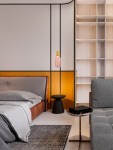 Lampa wisząca Perene z różowym kloszem i złotym detalem, zawieszona nad łóżkiem w nowoczesnym wnętrzu. Kształt owalny, materiał szklany, z widocznym przewodem. Tło w odcieniach bieli i pomarańczy, z minimalistycznym meblem obok.
