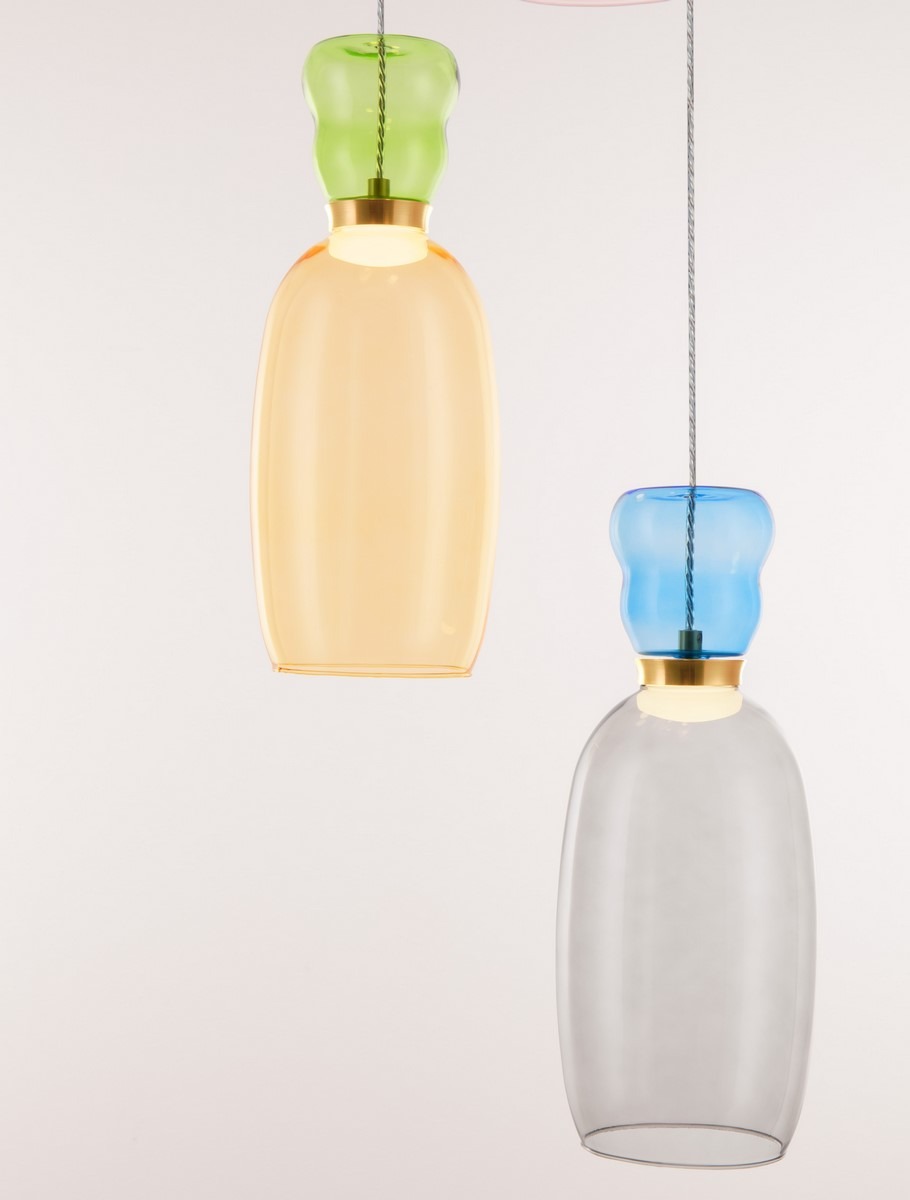 Lampa wisząca Perene z czterema kloszami LED w kolorze zielonym, pomarańczowym i niebieskim, z metalowymi detalami. Klosze mają kształt butelek, wiszące na cienkim przewodzie. Tło jasne, minimalistyczne.