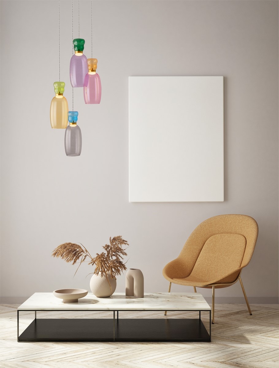 Lampa wisząca Perene, czarna, z czterema kolorowymi kloszami LED w odcieniach zielonym, różowym, fioletowym i żółtym. Klosze mają kształt butelek i są zawieszone na cienkich kablach. Produkt umieszczony w jasnym wnętrzu z minimalistycznymi meblami.