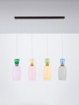 Lampa wisząca Perene z czterema kloszami LED w kolorach: fioletowym, różowym, żółtym i szarym, zawieszona na czarnej listwie. Klosze mają zaokrąglone kształty i ozdobne, kolorowe uchwyty. Lampa wisi na cienkich linkach w prostym otoczeniu.