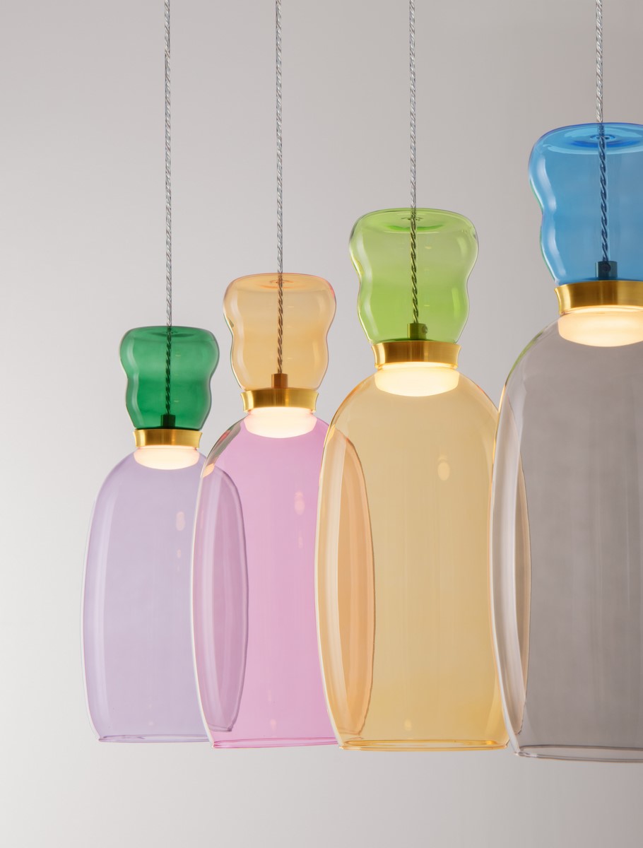Lampa wisząca Perene z czterema kloszami w różnych kolorach: zielonym, żółtym, różowym i fioletowym, zawieszona na cienkich linkach. Klosze mają zaokrąglony kształt i złote detale, emitując światło LED. Tło jasne, neutralne.