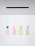 Lampa wisząca Perene z czterema kloszami LED w różnych kolorach: różowym, żółtym, zielonym i przezroczystym. Klosze mają zaokrąglony kształt, zawieszone na cienkich linkach z czarną metalową podstawą. Tło proste, białe.