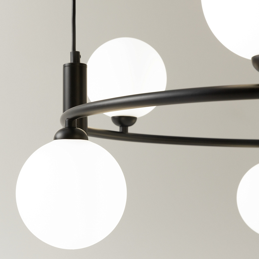 Czarna lampa wisząca Ring z sześcioma punktami świetlnymi. Metalowa konstrukcja z okrągłymi, matowymi kloszami w kolorze białym. Ujęcie z bliska, ukazujące detale mocowania i kształt kloszy.