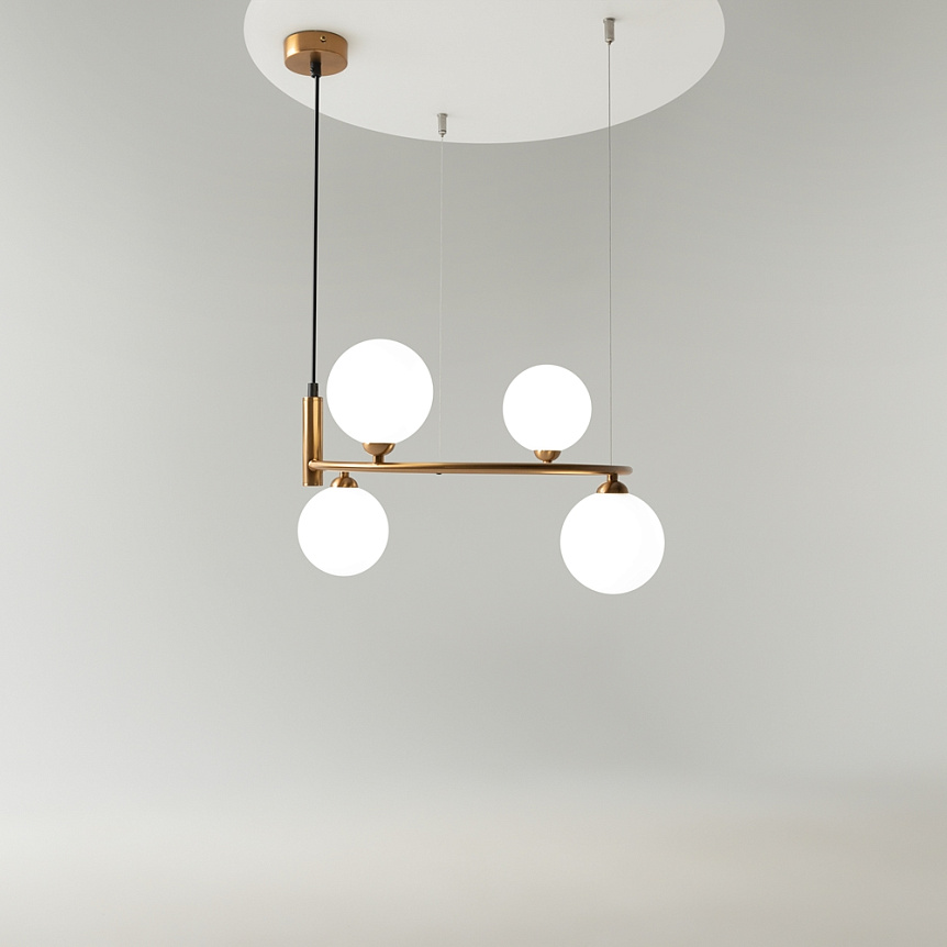 Lampa wisząca Ring 4-punktowa w kolorze mosiądzu, z czterema okrągłymi, białymi kloszami. Montowana sufitowo, z poziomym ramieniem. Prosta, nowoczesna konstrukcja na czarnych kablach, w minimalistycznym otoczeniu.
