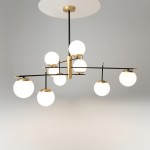 Lampa wisząca Nostalgia 9-punktowa w kolorze złotym. Posiada osiem okrągłych, białych kloszy, umieszczonych na czarnych, metalowych ramionach. Ujęcie frontalne, wisząca konstrukcja na prostym stelażu. Tło szare, jednolite.