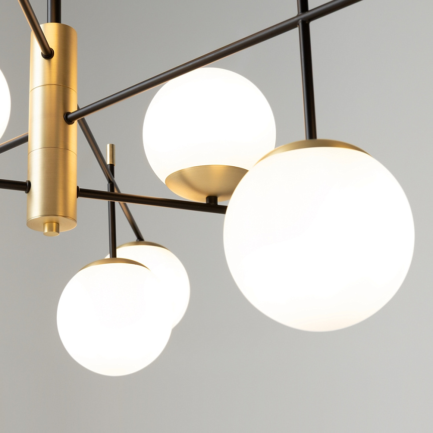 Lampa wisząca Nostalgia 9-punktowa w kolorze złotym. Konstrukcja z metalowymi ramionami i białymi, okrągłymi kloszami. Widok z bliska, ukazujący detal mocowania i kształt kulistych kloszy. Tło jednolite, jasne.