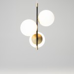 Lampa wisząca Nostalgia 3-punktowa, złota, z trzema okrągłymi kloszami w białym kolorze, zawieszona na cienkim czarnym stelażu. Klosze umieszczone w różnych wysokościach, z metalowymi elementami dekoracyjnymi. Prosty, nowoczesny design na jasnym tle.