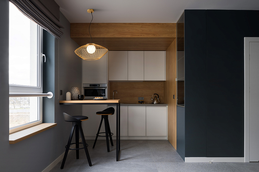 Złota lampa wisząca 1-punktowa Plec P364PL-01G, o ażurowym kształcie, zawieszona nad blatem w nowoczesnej kuchni. Widoczne elementy to czarne krzesła barowe oraz minimalistyczne meble w odcieniach bieli i drewna.