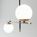 Lampa wisząca Nostalgia 2-punktowa w kolorze złotym. Dwie okrągłe, białe klosze zawieszone na czarnym stelażu, z metalowymi detalami. Klosze umieszczone na różnych wysokościach, tworzą nowoczesną kompozycję. Tło jasne, proste.