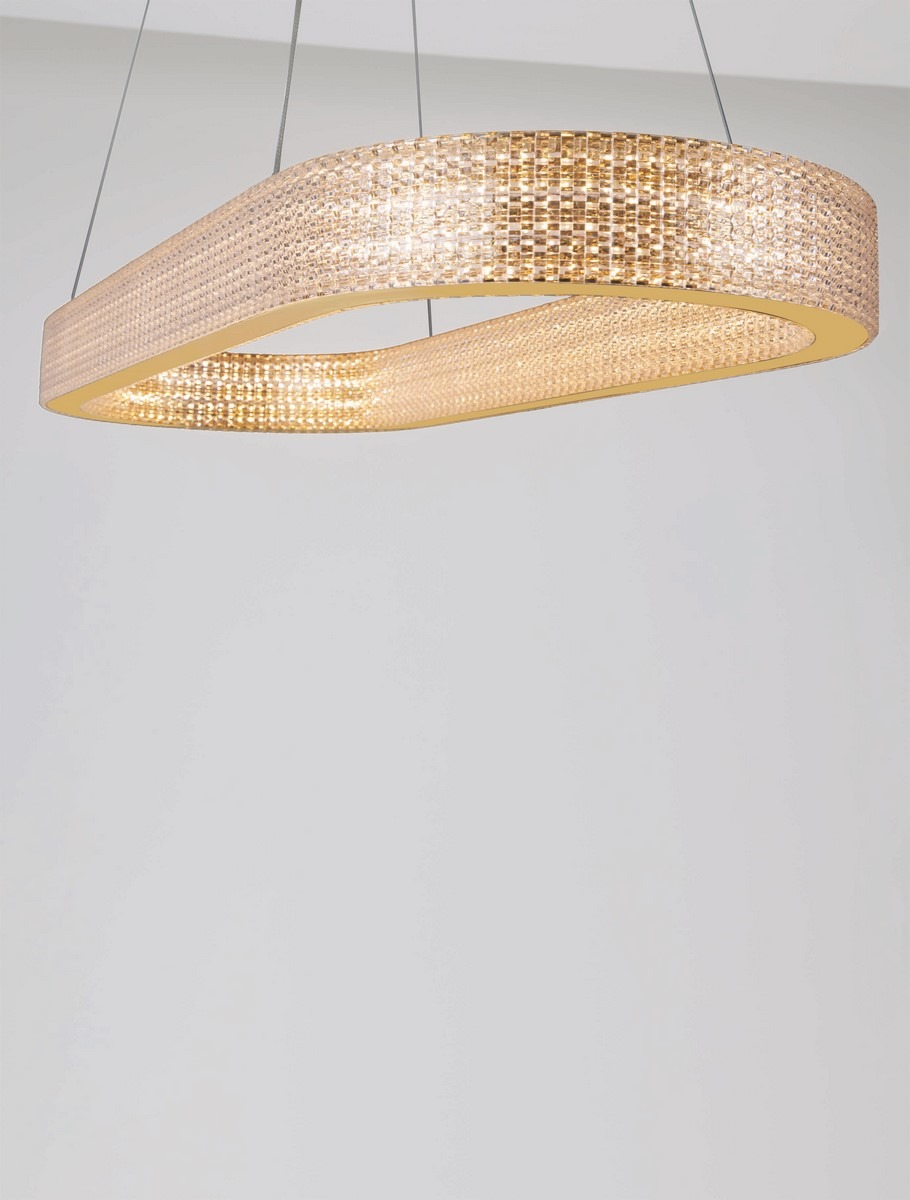 Złota lampa wisząca Yotau z 1xLED 70W, w kształcie falistego prostokąta. Wykonana z przezroczystego materiału, z dekoracyjnym wzorem, zawieszona na cienkich linkach. Oświetlenie wytwarza ciepłe, rozproszone światło. Tło w jasnym kolorze.