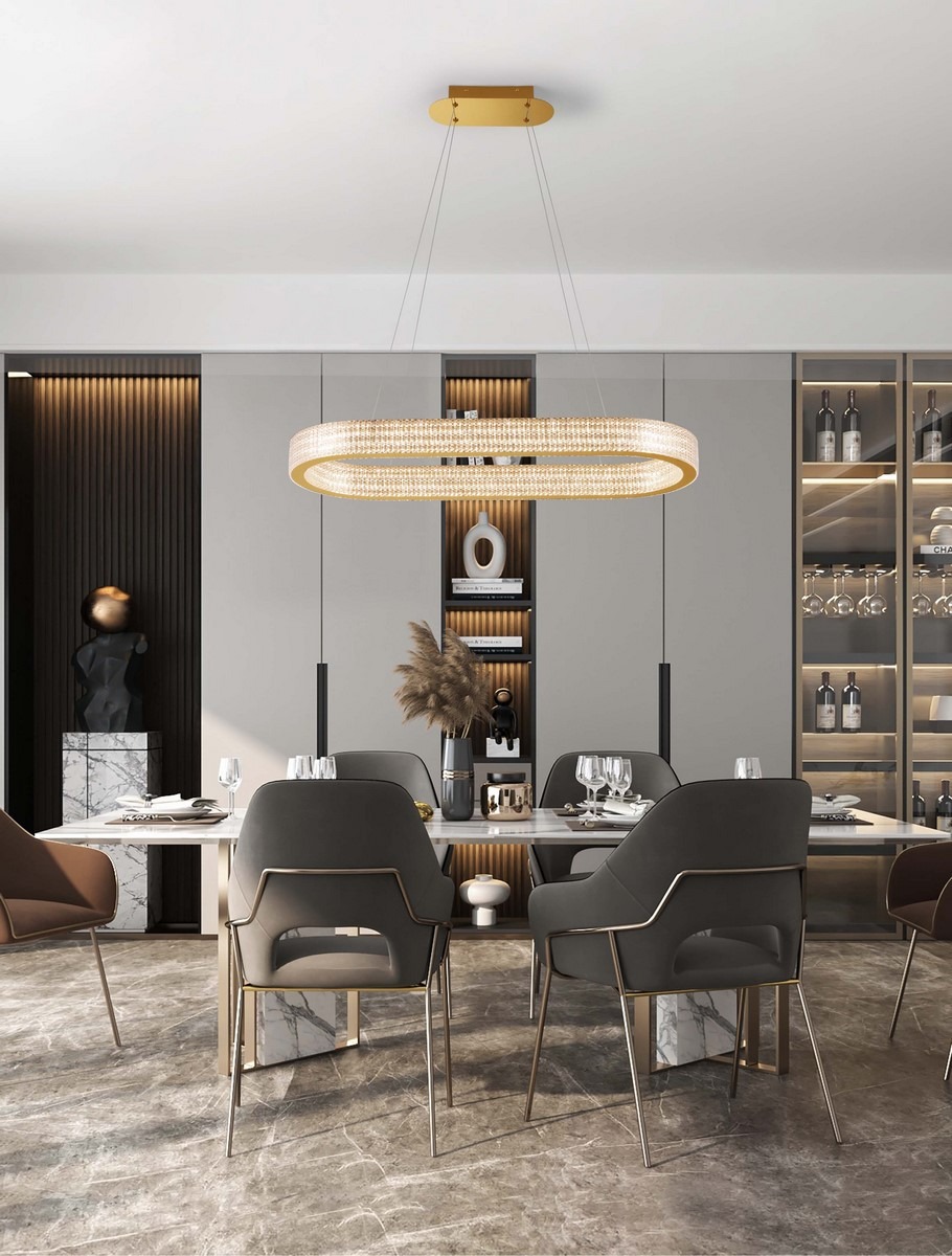 Lampa wisząca Yotau 1xLED 70W w kolorze złotym, o owalnym kształcie, zawieszona na cienkich linkach. W tle nowoczesna jadalnia z drewnianymi akcentami, szklanymi półkami i eleganckimi krzesłami. Złote detale podkreślają styl aranżacji.