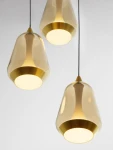 Lampa wisząca Rorizno z trzema kloszami, wykonana z przezroczystego szkła w odcieniu szampańskim. Klosze mają złote detale i emitują światło LED 24W. Zawieszona na czarnym przewodzie, w aranżacji na jasnym tle.