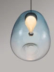 Lampa wisząca Jarevia z 1xLED 3W, czarna, z jasnoniebieskim kloszem w kształcie kropli. Zawieszona na cienkim kablu, z widocznym źródłem światła w centralnej części. Tło w odcieniach szarości, podkreślające elegancki design.