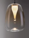 Lampa wisząca Jarevia 1xLED 3W w kolorze czarnym z bursztynowym kloszem, o zaokrąglonym kształcie. Zawieszona na cienkim przewodzie, z widoczną żarówką LED w centralnej części, tworzy efektowne źródło światła. Tło szare, proste.