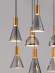Lampa wisząca Sarduno z siedmioma źródłami LED, o mocy 47W, w przydymionym szarym kolorze z elementami w złotym wykończeniu. Kształty kloszy w formie stożków i półkul, zawieszone na czarnych przewodach. Tło jasnoszare.