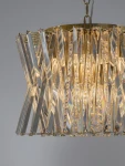 Lampa wisząca Melunto 8xE14 w satynowym mosiądzu. Ozdobna konstrukcja z przezroczystych, błyszczących elementów, układających się w geometryczny wzór. Zbliżenie na detale, widoczne żarówki w środku, wisząca na łańcuszku. Tło szare.