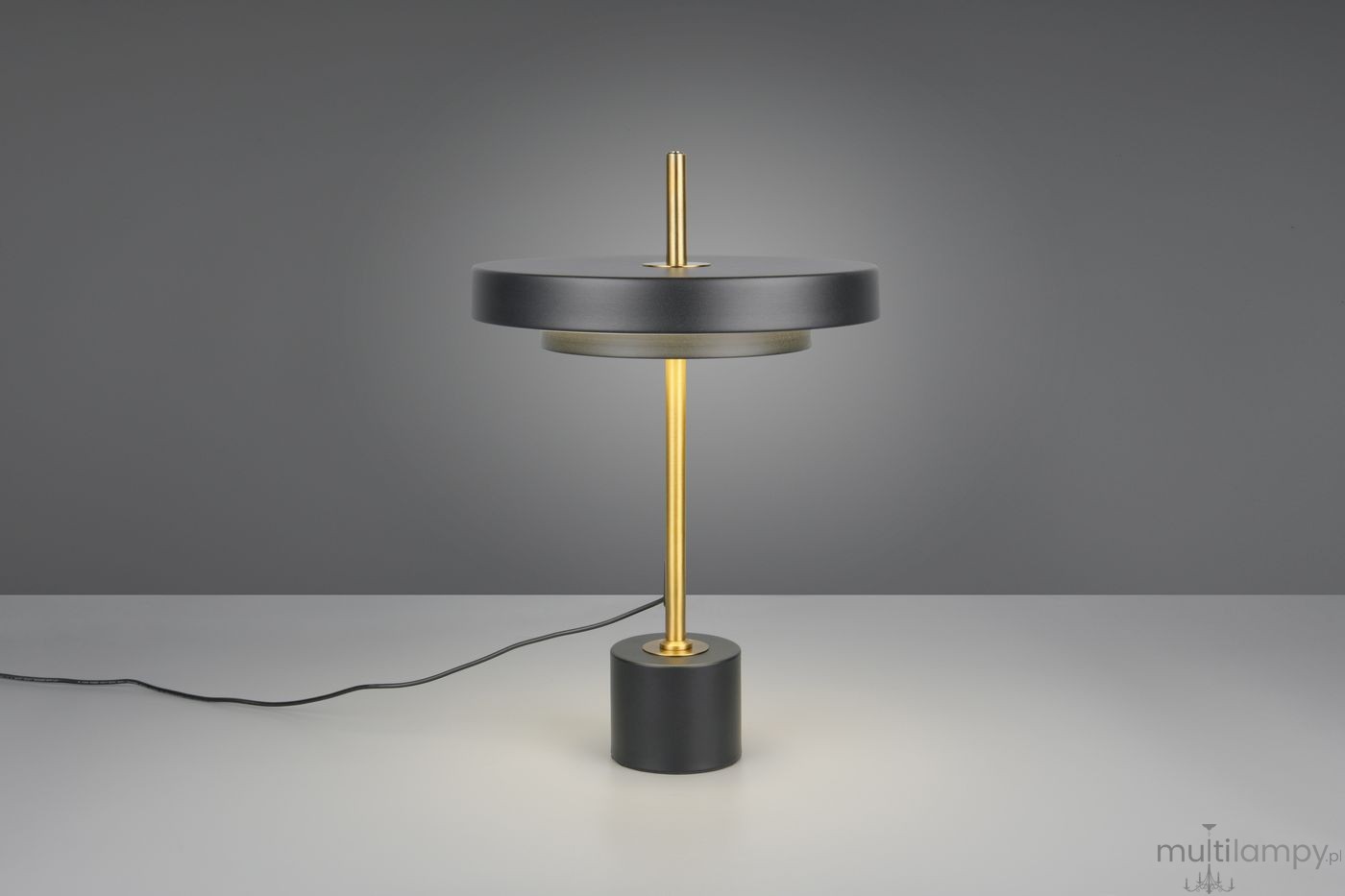 Lampa stołowa Keaton w kolorze czarnym i złotym, z podstawą w kształcie walca. Posiada okrągły klosz oraz metalowy stelaż. Ujęcie frontalne, prezentujące całość lampy z widocznym przewodem zasilającym. Wbudowany moduł LED 12W.