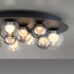 Lampa sufitowa Pure Popup, grafitowa, z 11 okrągłymi kloszami z przezroczystego szkła, emitującymi ciepłe światło. Zainstalowana na okrągłej, matowej podstawie. W komplecie pilot do zdalnego sterowania.