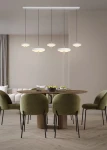 Lampa wisząca Keaton z pięcioma okrągłymi kloszami LED w kolorze szarym, zawieszona na cienkich linkach. Umieszczona nad okrągłym stołem w jadalni, obok zielonych foteli, na tle jasnej ściany i zasłon.