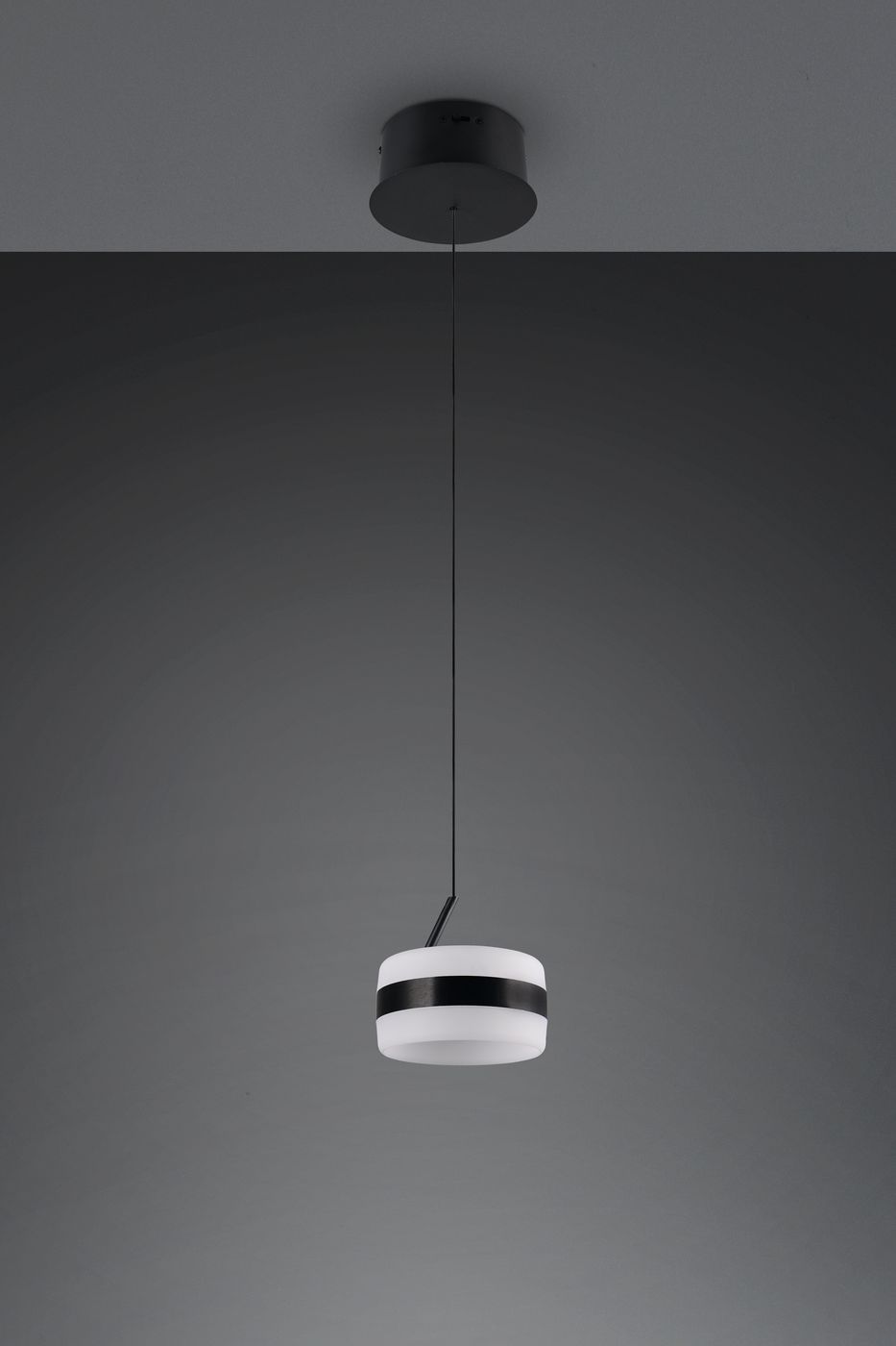 Lampa wisząca Dios z jednym źródłem LED 8W, w kolorze czarnym, z okrągłym kloszem z białego materiału i czarną opaską. Zawieszona na cienkim przewodzie, umieszczona pod sufitem, na jednolitym tle.