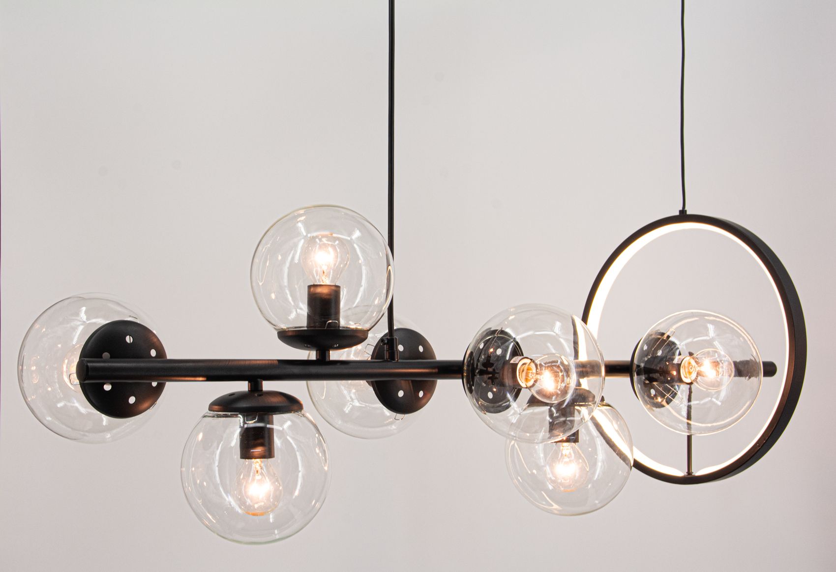 Czarna lampa wisząca Galaxy z siedmioma oprawami E14 i jedną LED. Szklane klosze w kształcie kul, metalowa konstrukcja, okrągły element LED w górnej części. Ujęcie frontalne, produkt zawieszony na cienkim przewodzie, na jasnym tle.