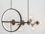 Lampa wisząca Galaxy w kolorze czarnym, z siedmioma gniazdami E14 oraz jednym LED. Okrągły, matowy metalowy element z białym podświetleniem i sześcioma przezroczystymi kloszami, w których znajdują się żarówki, zawieszona na długim kabelku.
