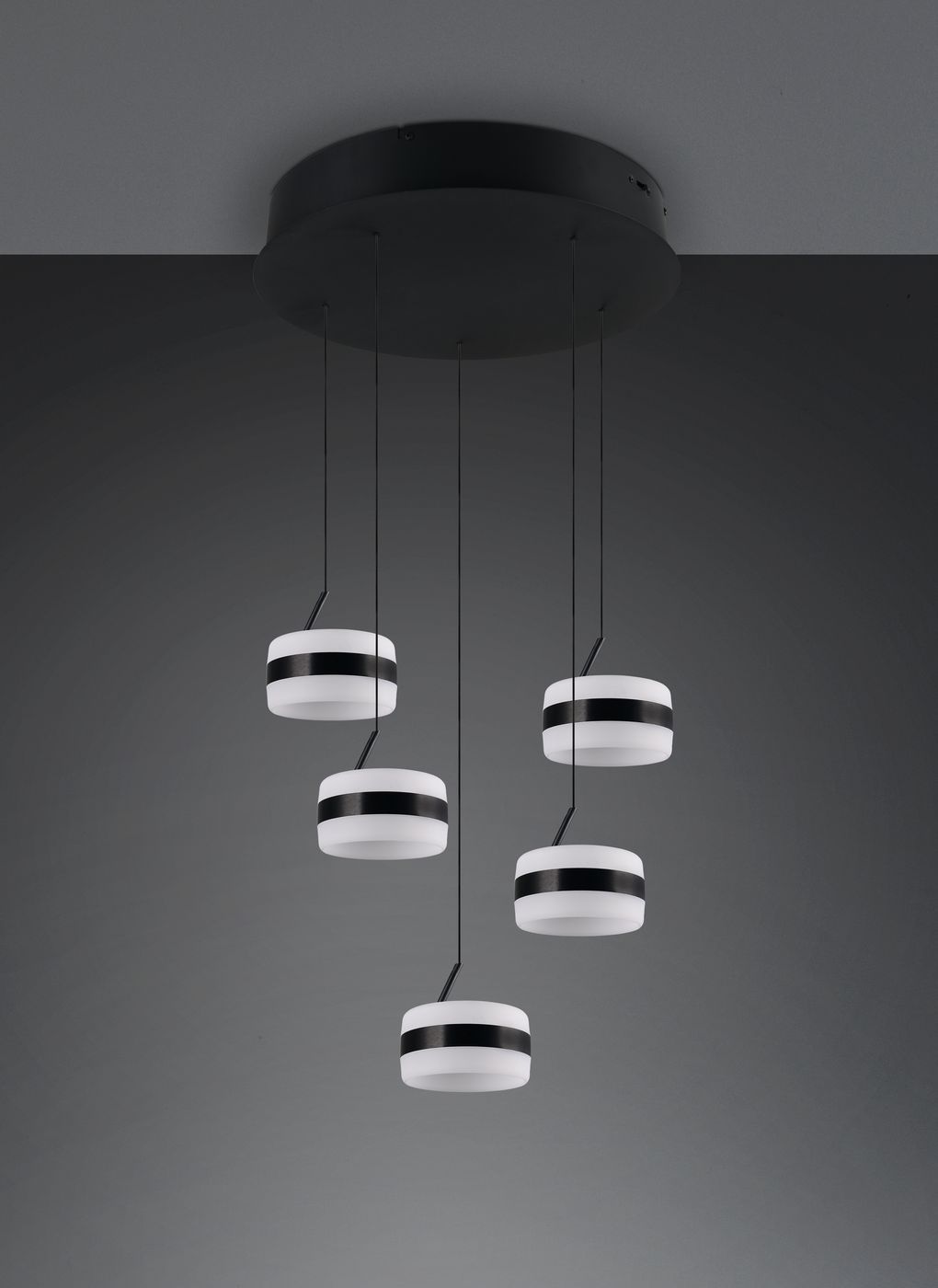 Lampa wisząca Dios z pięcioma źródłami LED o mocy 40W, w kolorze czarnym. Okrągłe klosze z białym wykończeniem i czarnymi paskami, zawieszone na cienkich linkach, montowane na okrągłej podsufitce. Tło szare, minimalistyczne.