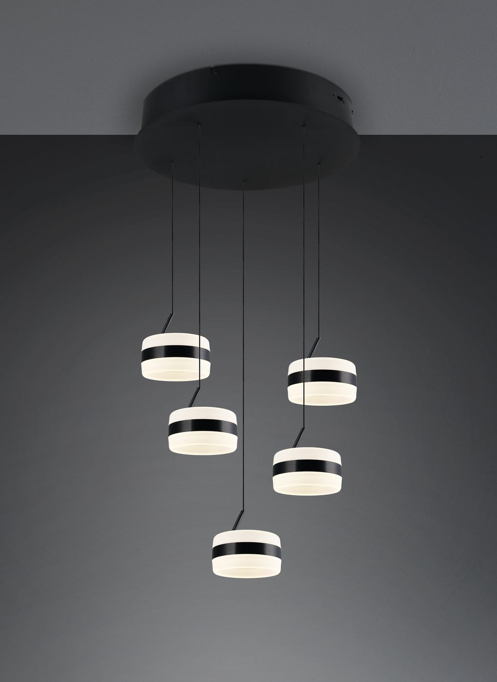 Lampa wisząca Dios z pięcioma okrągłymi kloszami LED, w czarnej obudowie. Klosze mają biało-czarne paski, zawieszone na cienkich linkach, montowane do okrągłego podsufitki. Zdjęcie na ciemnym tle, podkreślającym kontrast lampy.
