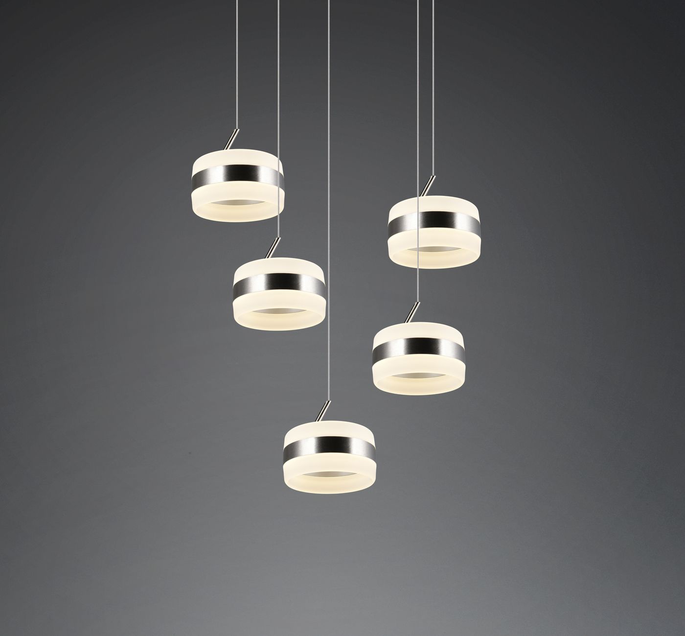 Lampa wisząca Dios z pięcioma źródłami LED w kolorze niklu. Okrągłe klosze z białym, półprzezroczystym szkłem, zawieszone na cienkich linkach. Prosty, nowoczesny design, idealna do różnych wnętrz. Tło w odcieniach szarości.