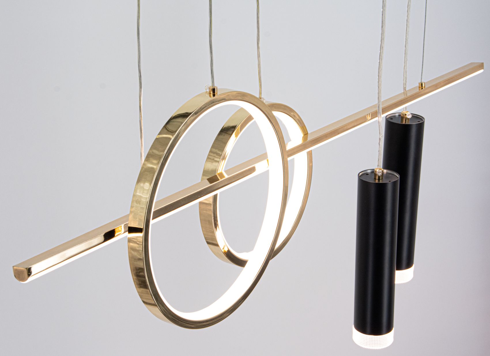Lampa wisząca Moderno z metalową konstrukcją w kolorze złotym, z dwoma okrągłymi elementami i trzema cylindrycznymi oprawami w kolorze czarnym. Zintegrowane oświetlenie LED oraz miejsce na żarówki E14. Zawieszona na cienkich linkach, w nowoczesnym stylu.