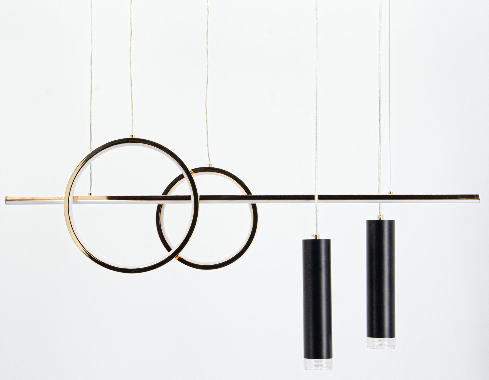 Lampa wisząca Moderno z dwoma złotymi okręgami i trzema czarnymi cylindrami LED. Zawieszona na białych linkach, wyróżnia się minimalistycznym designem. Okręgi mają połyskującą złotą powierzchnię, a cylindry są matowe z metalowymi elementami.