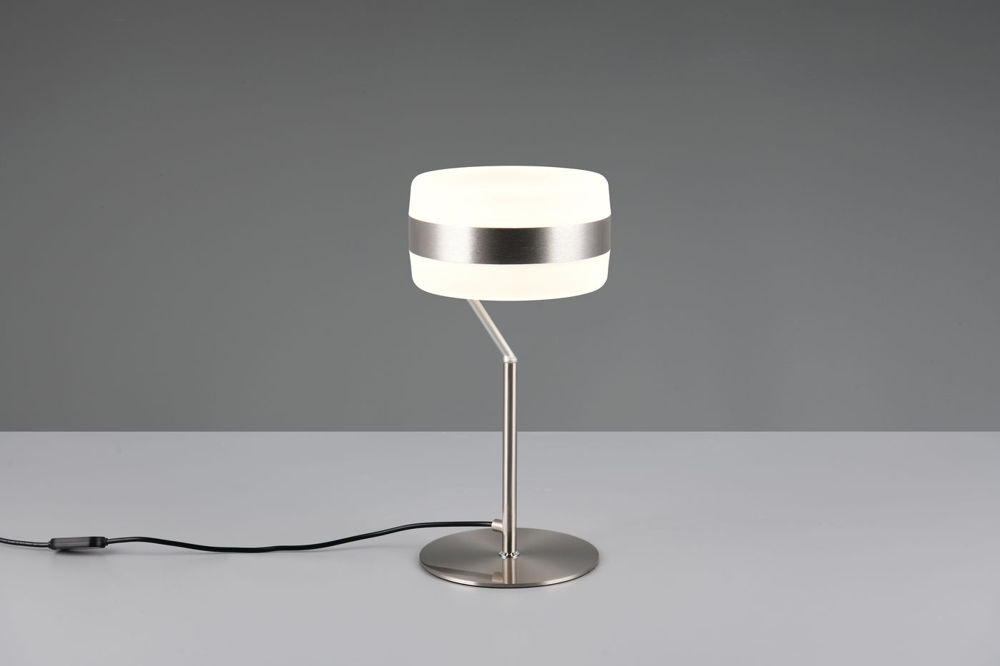 Lampa stołowa Dios z niklowanym stelażem, z okrągłą podstawą. Klosz z mlecznego szkła z metalowym paskiem. Ujęcie frontalne, widoczny kabel z włącznikiem. Wymiary: wysokość około 40 cm, średnica klosza 15 cm.